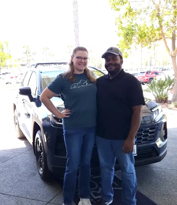 Two clients standing in front of their new Toyota RAV4 at the dealership