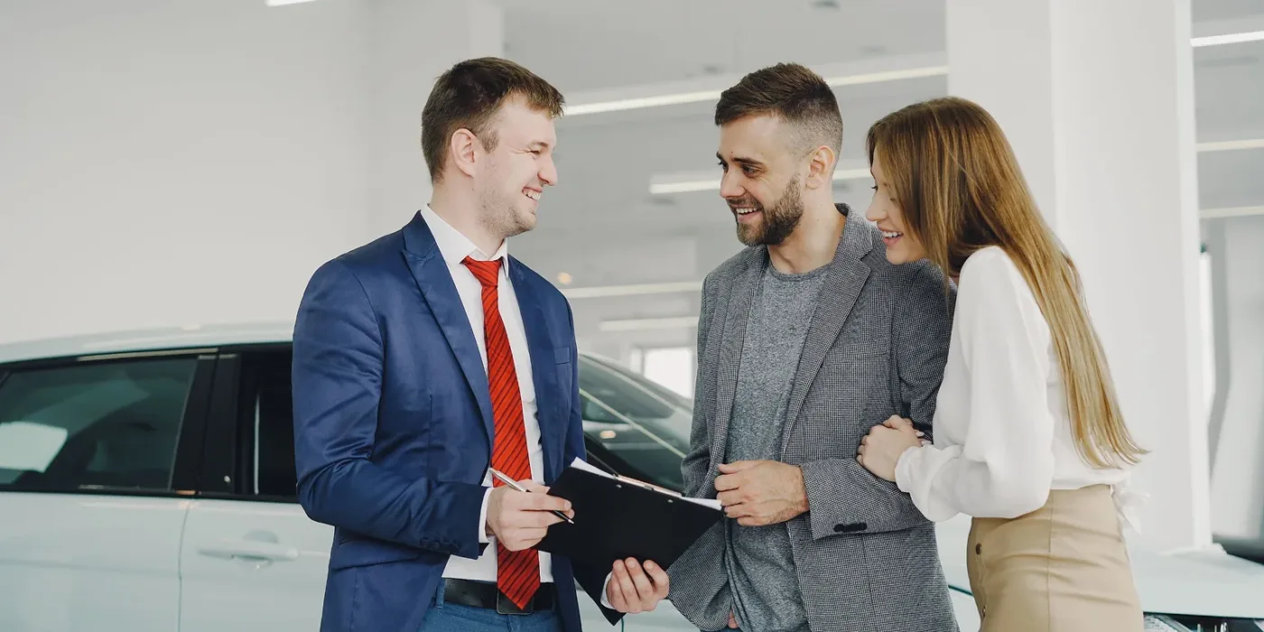A smiling couple going over the lease paperwork with a car salesman in a bright showroom